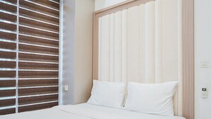 A hotel room with a bed, a window with blinds, and a light switch on the wall.