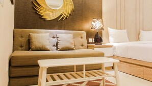 A modern hotel room with a sofa, a bed, a bedside table, a lamp, and a unique wall mirror.