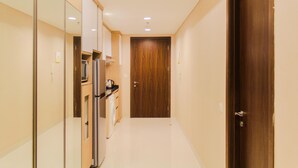 A narrow hallway with a wooden door at the end, a refrigerator, and a microwave on a counter.