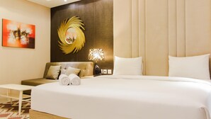 A hotel room with a large bed, a sofa, a small table, and a wall with a decorative mirror and artwork.