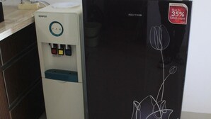 A kitchen with a water dispenser and a black refrigerator with a floral design. - Comfy 2Br Apartment At Park View Condominium (Depok)