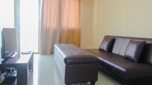 A living room with a dark brown leather sofa, a matching ottoman, and a flat-screen TV on a stand. - Comfy 2Br Apartment At Park View Condominium (Depok)