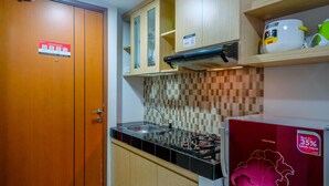 A compact kitchen with wooden cabinets, a tiled backsplash, a stainless steel sink, and a red appliance with a flower design. - Comfy And Modern Margonda Residence 5 Studio Apartment (Depok)