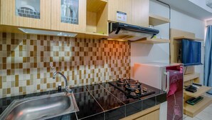 A kitchen with a black countertop, stainless steel sink, and a gas stove. There are wooden cabinets and a tiled backsplash. - Comfy And Modern Margonda Residence 5 Studio Apartment (Depok)