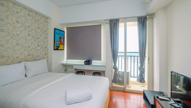 A hotel room with a bed, a desk, a TV, and a balcony with curtains.