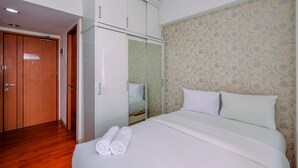 A hotel room with a wooden floor, a bed with white bedding, a wardrobe with mirrored doors, and floral wallpaper.