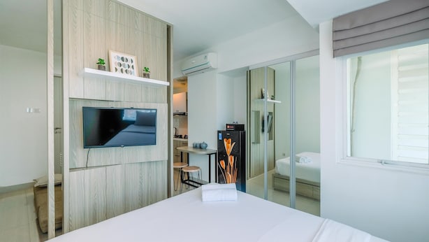Een moderne hotelkamer met een groot bed, een flatscreen-televisie aan de muur bevestigd, een klein kitchenette en een schuifdeur naar een badkamer.