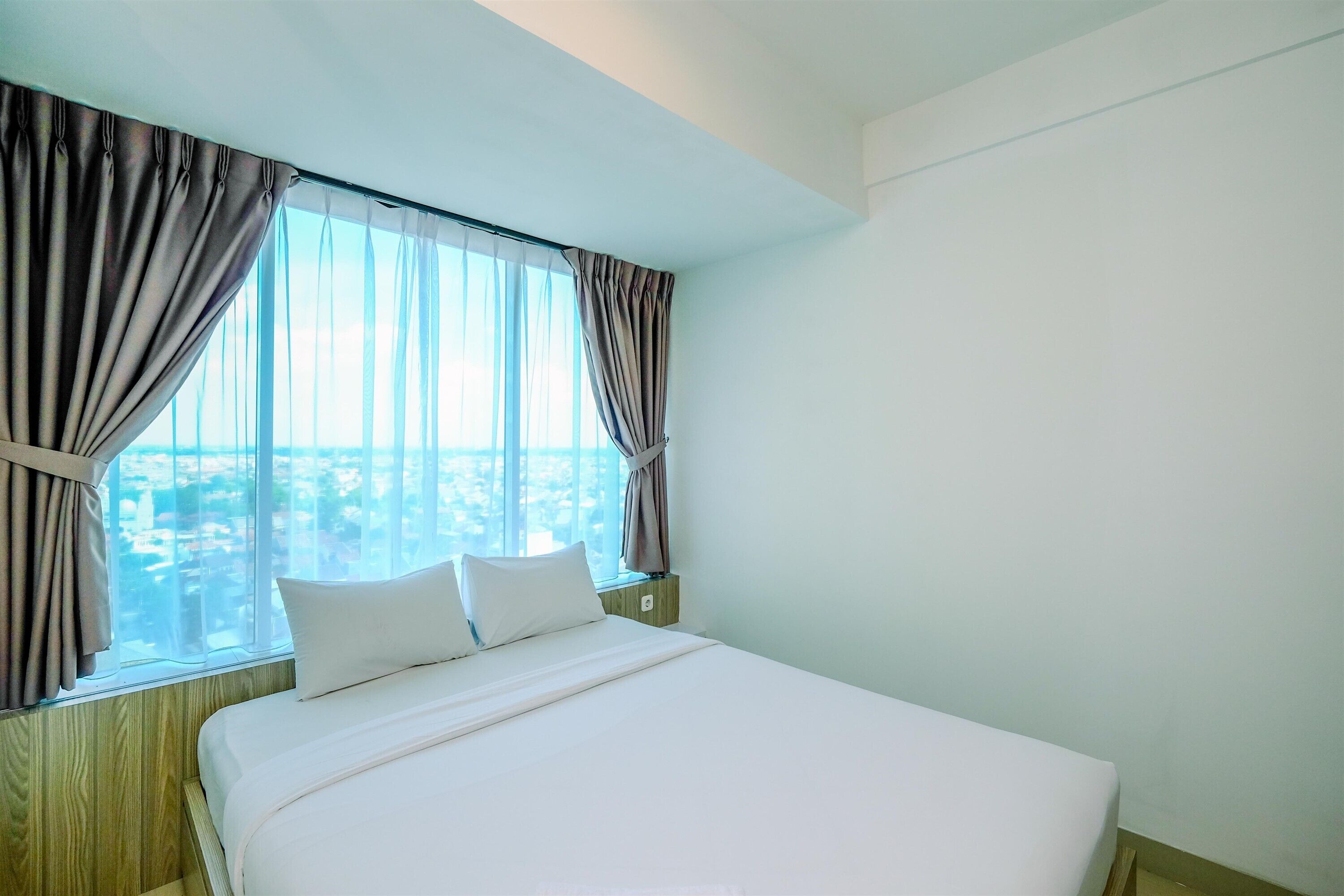 A hotel room with a large bed, a view of the city through the window, and curtains on the window.