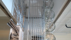 Een keuken met een ingebouwde vaatwasser en een metalen rek met helder glazen servies.