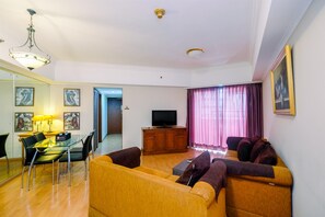 A living room with a sofa, TV, wooden cabinet, and a dining table with chairs.