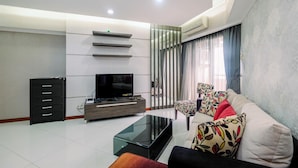 A modern living room with a flat-screen TV, a glass coffee table, a sofa, and a cabinet. - Spacious For 2Br Apartment At Sudirman Tower Condominium (Jakarta)