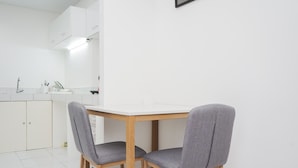A modern kitchen with white cabinets, a white countertop, and two grey upholstered chairs. - Simply 1Br At Casa De Parco Apartment (Pagedangan)