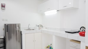 A modern kitchen with white cabinetry, a stainless steel refrigerator, a sink, and a kettle on the countertop. - Simply 1Br At Casa De Parco Apartment (Pagedangan)