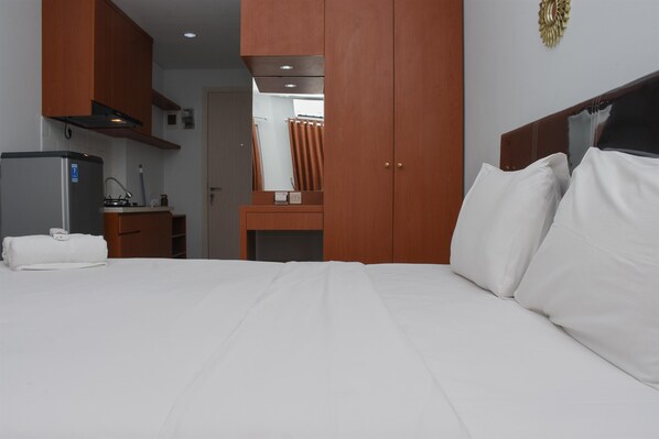 Une chambre d’hôtel avec un lit, une armoire en bois, une petite kitchenette et un miroir.