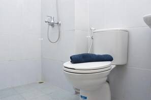 Des toilettes blanches avec une serviette bleue posée sur le couvercle, une pomme de douche et un porte-rouleau de papier toilette.