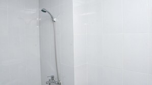 Doccia con soffione a mano e rubinetto a muro in un bagno piastrellato.