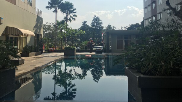Un espace piscine extérieur paisible, entouré de bâtiments modernes, agrémenté de palmiers et offrant une vue sur un ciel dégagé.
