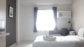 Une chambre d’hôtel avec un lit, un bureau, une chaise, une télévision et une fenêtre avec des rideaux.