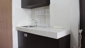 Une cuisine avec un plan de travail blanc, des meubles de couleur foncée, un évier blanc et une multiprise blanche.