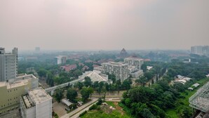 A high-rise building with a modern architectural design, surrounded by greenery and other buildings. - Cozy Stay Studio Apartment At Park View Condominium (Depok)