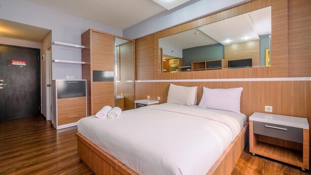 A modern hotel room with a large bed, wooden wardrobe, a mirror, and a small bedside table. - Cozy Stay Studio Apartment At Park View Condominium (Depok)