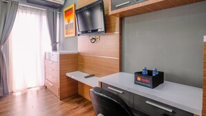 A modern hotel room with a wooden desk, a flat-screen TV, a minibar, and a black chair. - Cozy Stay Studio Apartment At Park View Condominium (Depok)