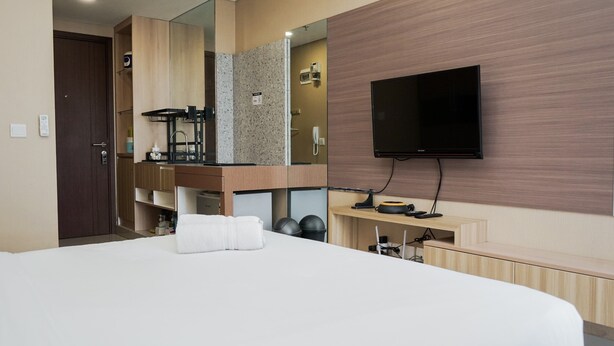 A modern hotel room with a large bed, a TV, a mirror, a sink, and a wooden vanity. - Best And Relax Studio Room Parkland Avenue Apartment (South Tangerang)