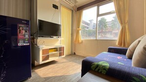 Habitación de hotel con una cama, un televisor montado en la pared, una mesita y una ventana con cortinas.