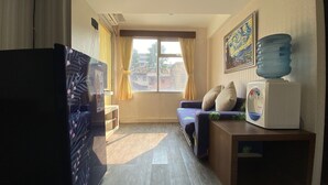Un espacio habitable compacto con sofá, una mesita con dispensador de agua, refrigerador y ventana con cortinas.