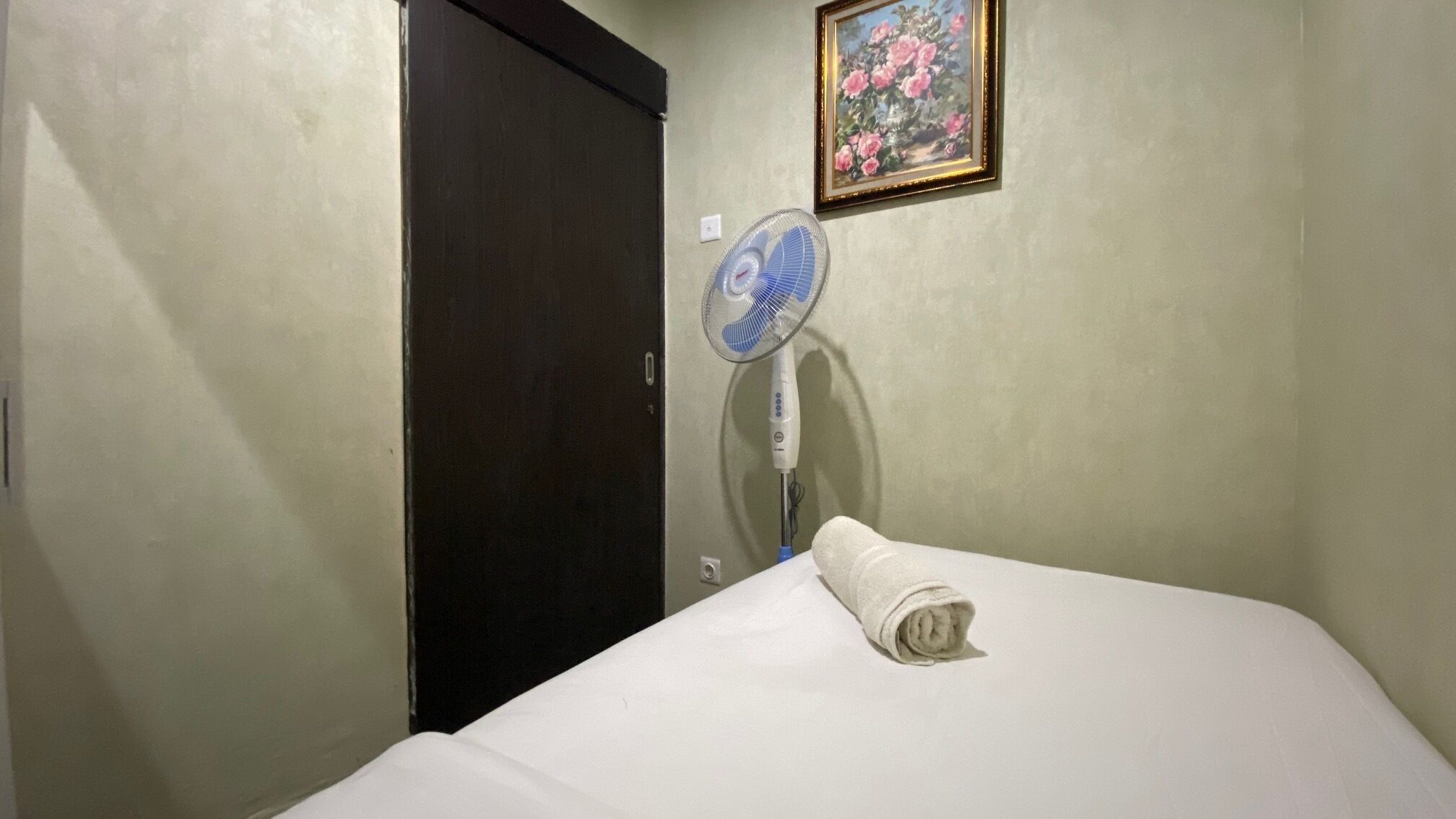 A hotel room with a bed, a wall-mounted fan, and a door.