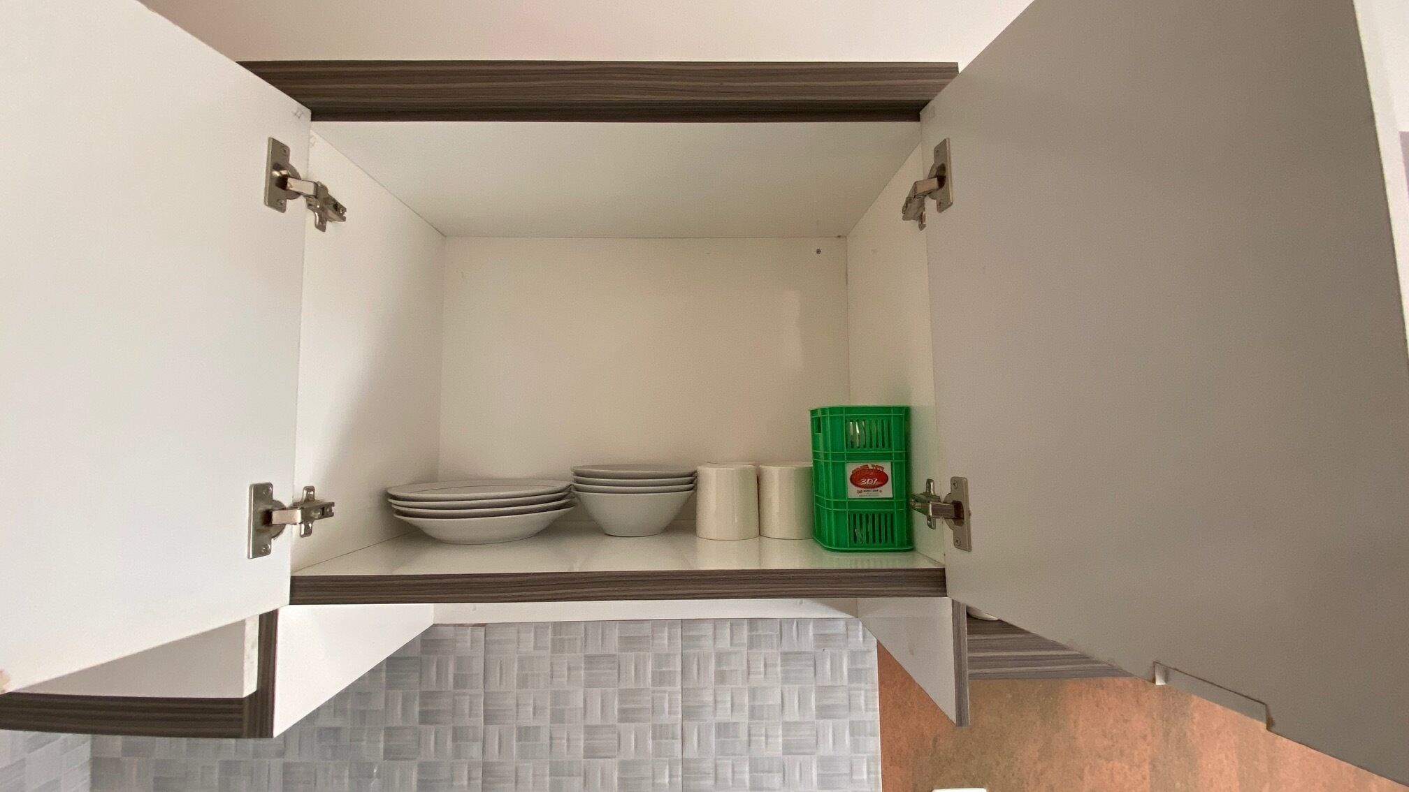 Una cocina con armarios blancos, salpicadero de azulejos y un contenedor verde para guardar objetos.