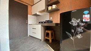 A compact kitchen with a refrigerator, a microwave, and a small stool. - Comfortable And Simply Modern 2Br Apartment At The Jarrdin Cihampelas (Bandung)