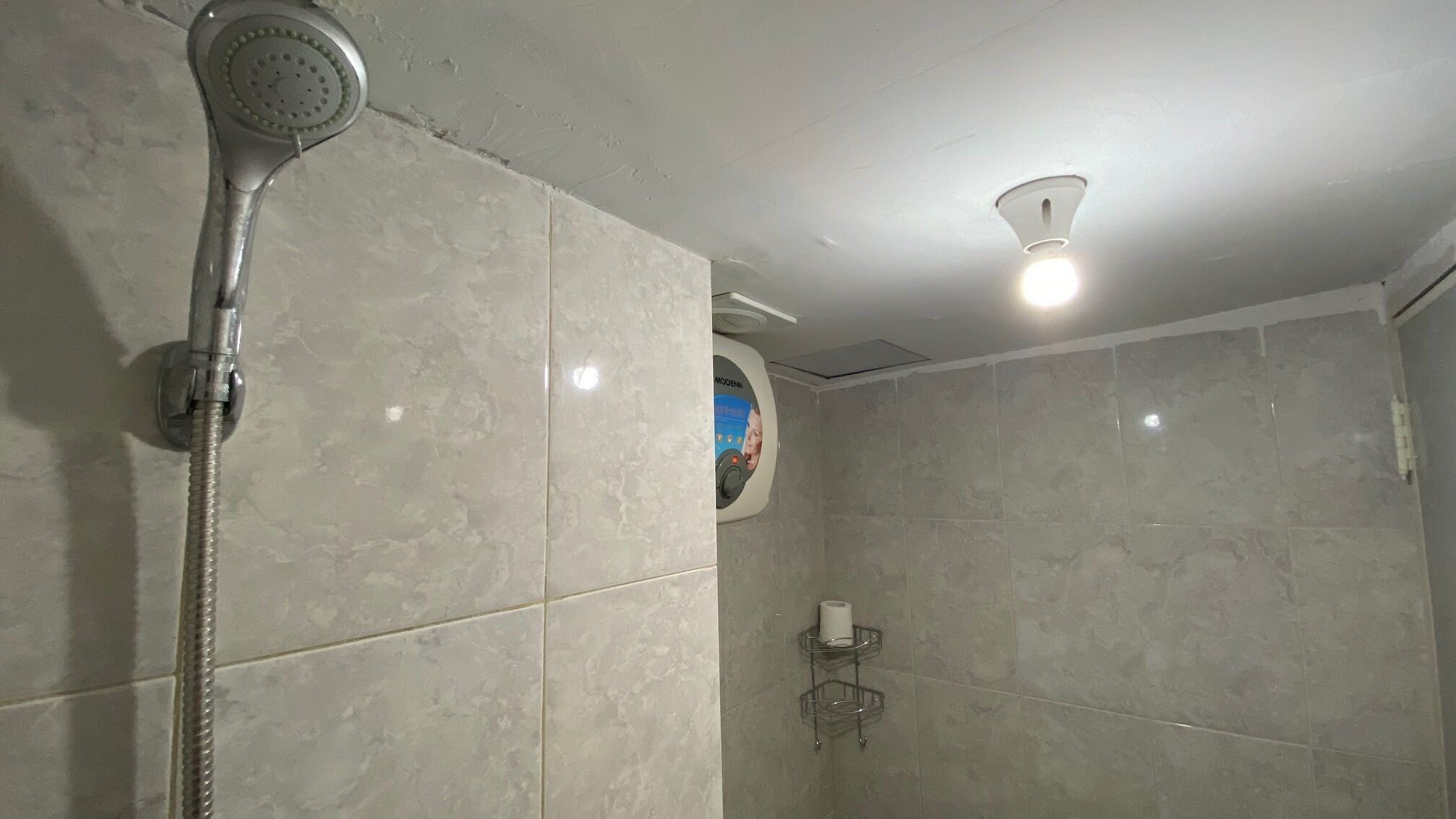 Ducha con cabezal de ducha de mano, panel de control en la pared y lámpara en el techo.