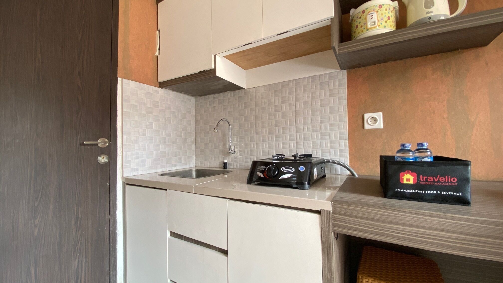 Une petite cuisine équipée d’un évier, d’une plaque de cuisson au gaz portable et d’une étagère contenant un sac de produits alimentaires et de boissons offerts.