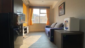 A compact room with a sofa, a small table, a refrigerator, and a window with curtains. - Comfortable And Simply Modern 2Br Apartment At The Jarrdin Cihampelas (Bandung)