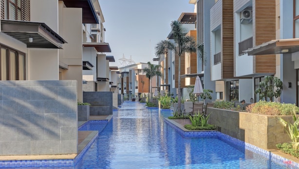 A modern residential building with a central swimming pool, surrounded by balconies and greenery. - Homey 2Br At Asatti Apartment (Pagedangan)