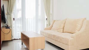 A modern living room with a beige sofa, a wooden coffee table, and a TV on a wooden stand. - Homey 2Br At Asatti Apartment (Pagedangan)