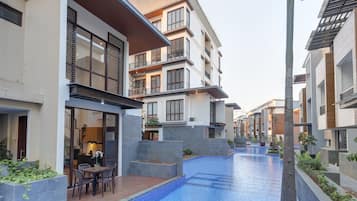 A modern residential building with a swimming pool, balconies, and a patio area with outdoor furniture.