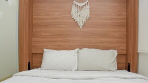 A bed with white bedding and a macrame wall hanging. - 2Br Yotayori Home At Green Pramuka City Apartment (Jakarta)