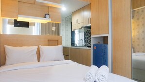 A hotel room with a bed, a neatly made bed with rolled towels, a small kitchenette with a refrigerator, and a mirror reflecting the room. - Exquisite Studio Apartment At Tamansari Papilio (Surabaya)