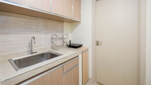 A kitchen with a stainless steel sink, wooden cabinets, and a door. - Cozy 2Br At Meikarta Apartment (Cikarang)