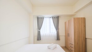 A bedroom with a bed, a wardrobe, and a window with curtains. - Cozy 2Br At Meikarta Apartment (Cikarang)