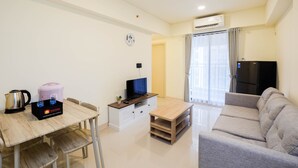 A modern living room with a sofa, a TV, a coffee maker, and a small table. - Cozy 2Br At Meikarta Apartment (Cikarang)