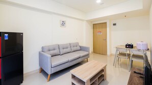 A modern living room with a grey sofa, a wooden coffee table, a black refrigerator, and a wooden door in the background. - Cozy 2Br At Meikarta Apartment (Cikarang)