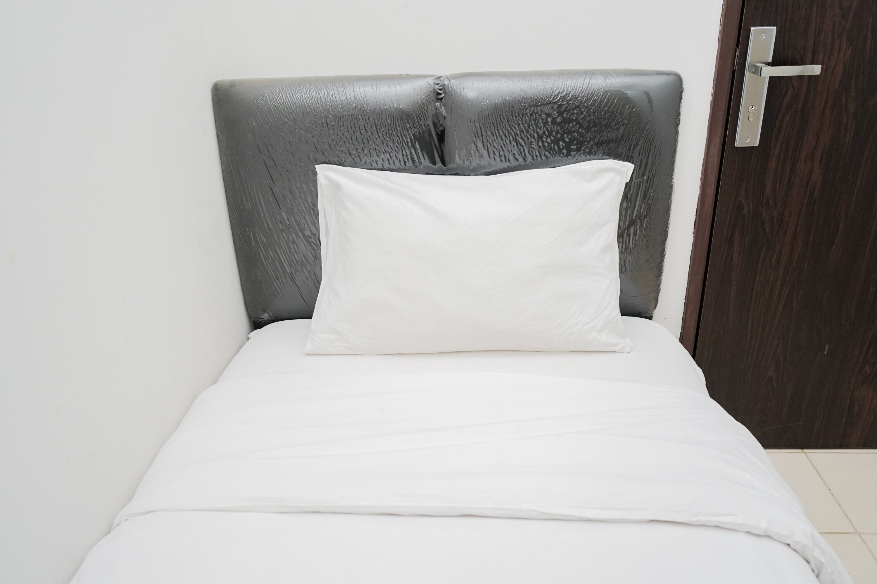 Un lit avec une tête de lit grise et un oreiller blanc.