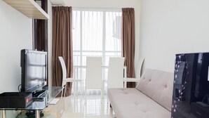 A modern living room with a sofa, two white chairs, a glass coffee table, a flat-screen TV, and a black entertainment unit. - Homey And Simply 2Br At Serpong Greenview Apartment (South Tangerang)