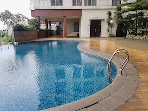 Une piscine dont le bord est revêtu de carreaux, avec une rambarde métallique, et un bâtiment doté d’un balcon en arrière-plan.