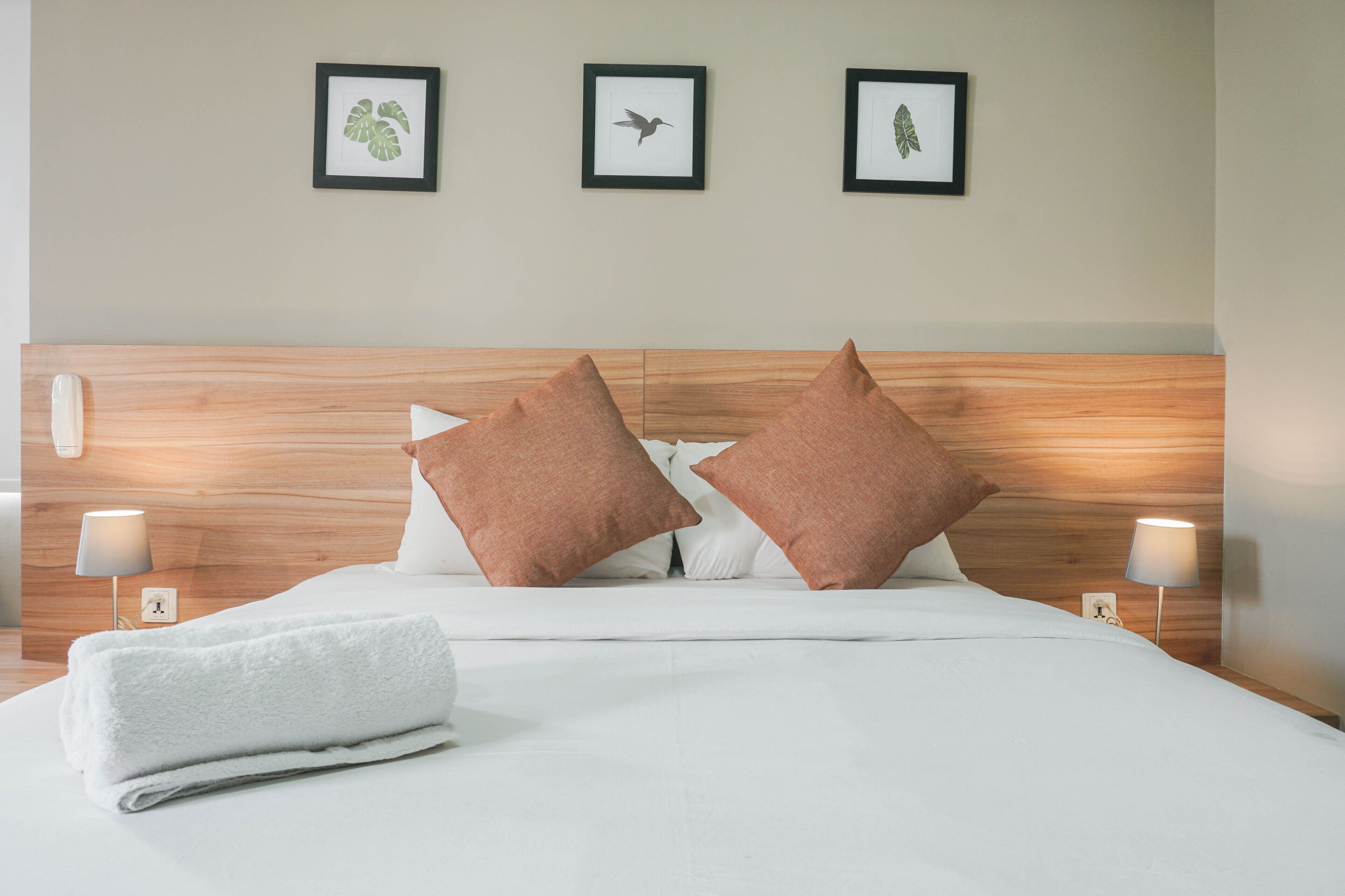 A neatly made bed with white linens and two brown pillows, a wooden headboard, and three framed pictures on the wall above.