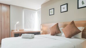 A hotel room with a large bed, two pillows, a bedside table with a lamp, a window with curtains, and framed pictures on the wall.