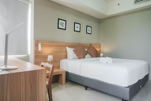 Une chambre d’hôtel moderne avec une tête de lit en bois, un grand lit avec une literie blanche, un bureau avec une lampe et une chaise. Trois tableaux encadrés ornent le mur.
